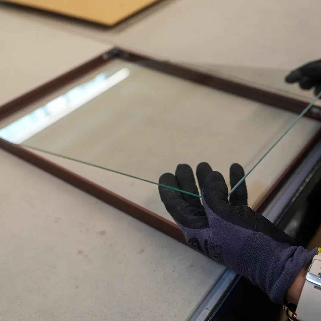 Mit Schutzhandschuhen wird eine Glasscheibe in einen dunklen Holzrahmen gelegt
