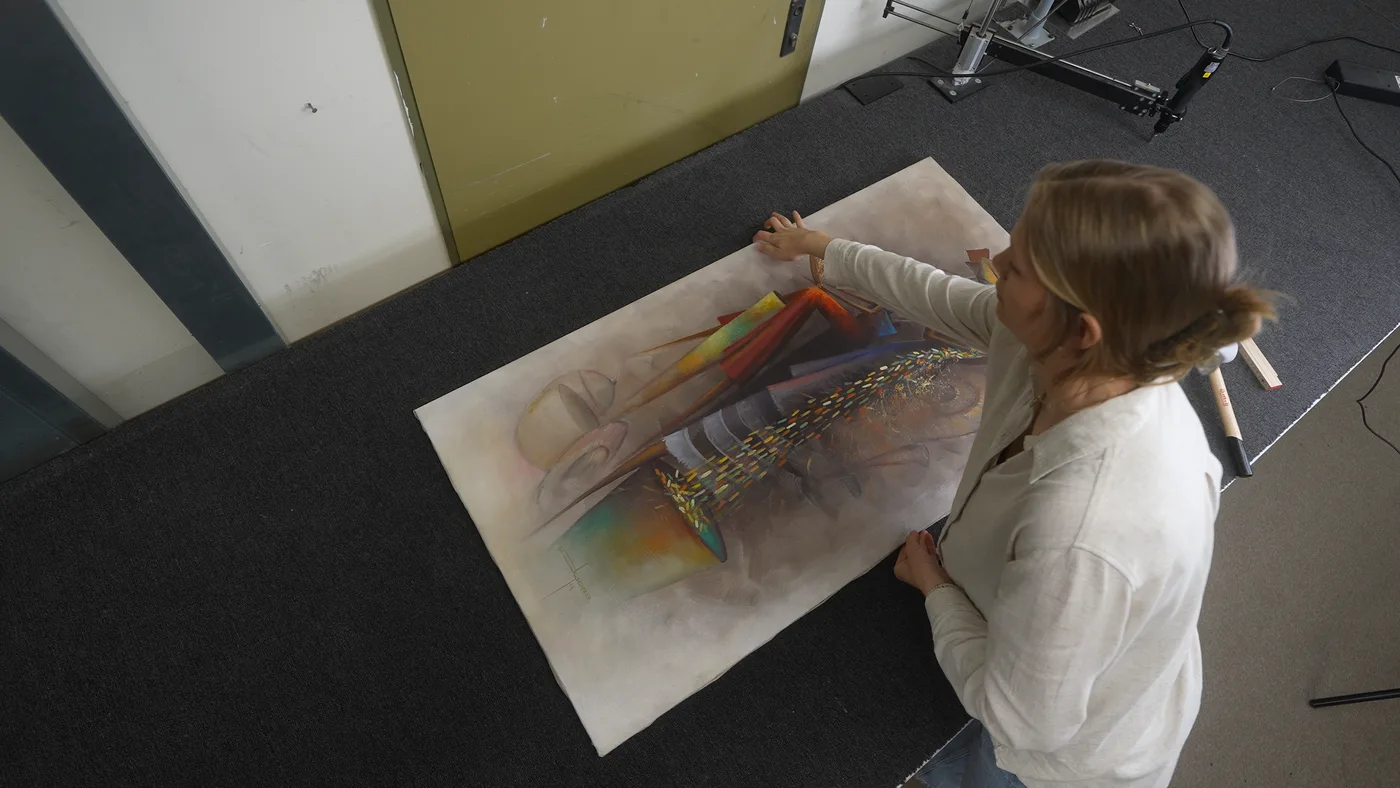 Fertig gespannte Leinwand wird vom Werkstatttisch hochgehalten