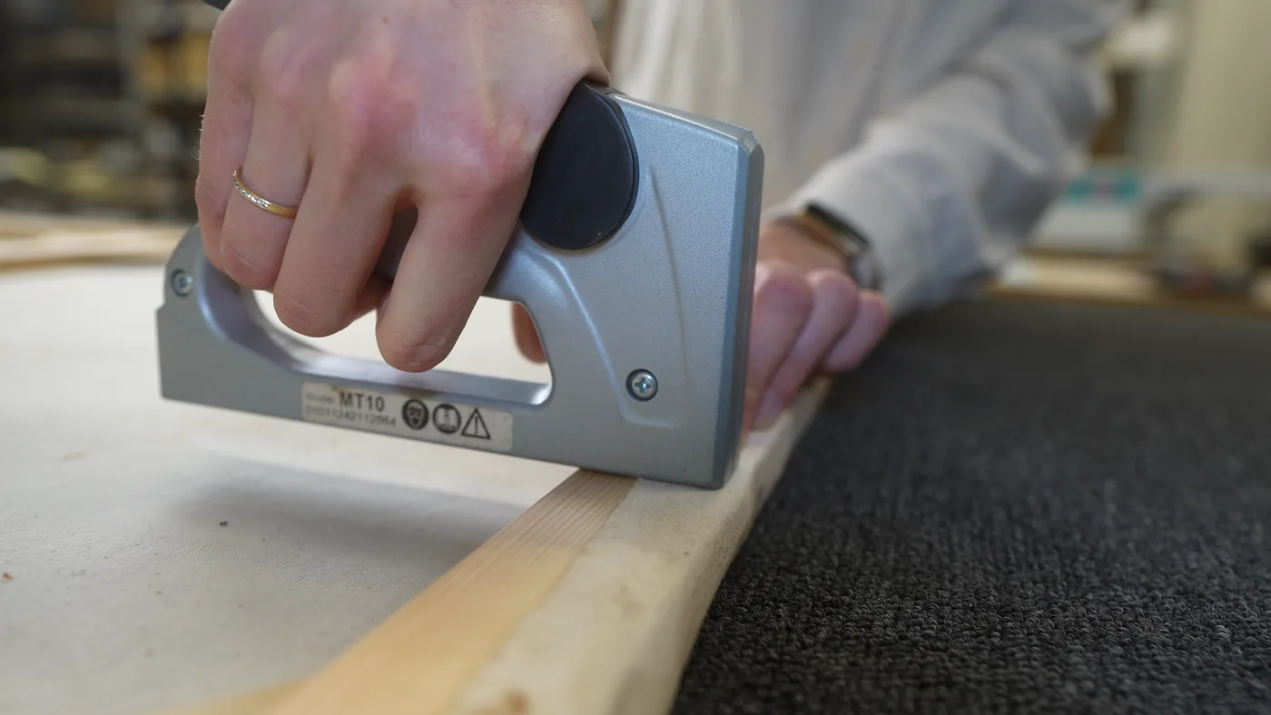 Handtacker setzt eine Klammer in die Leiste des Keilrahmens