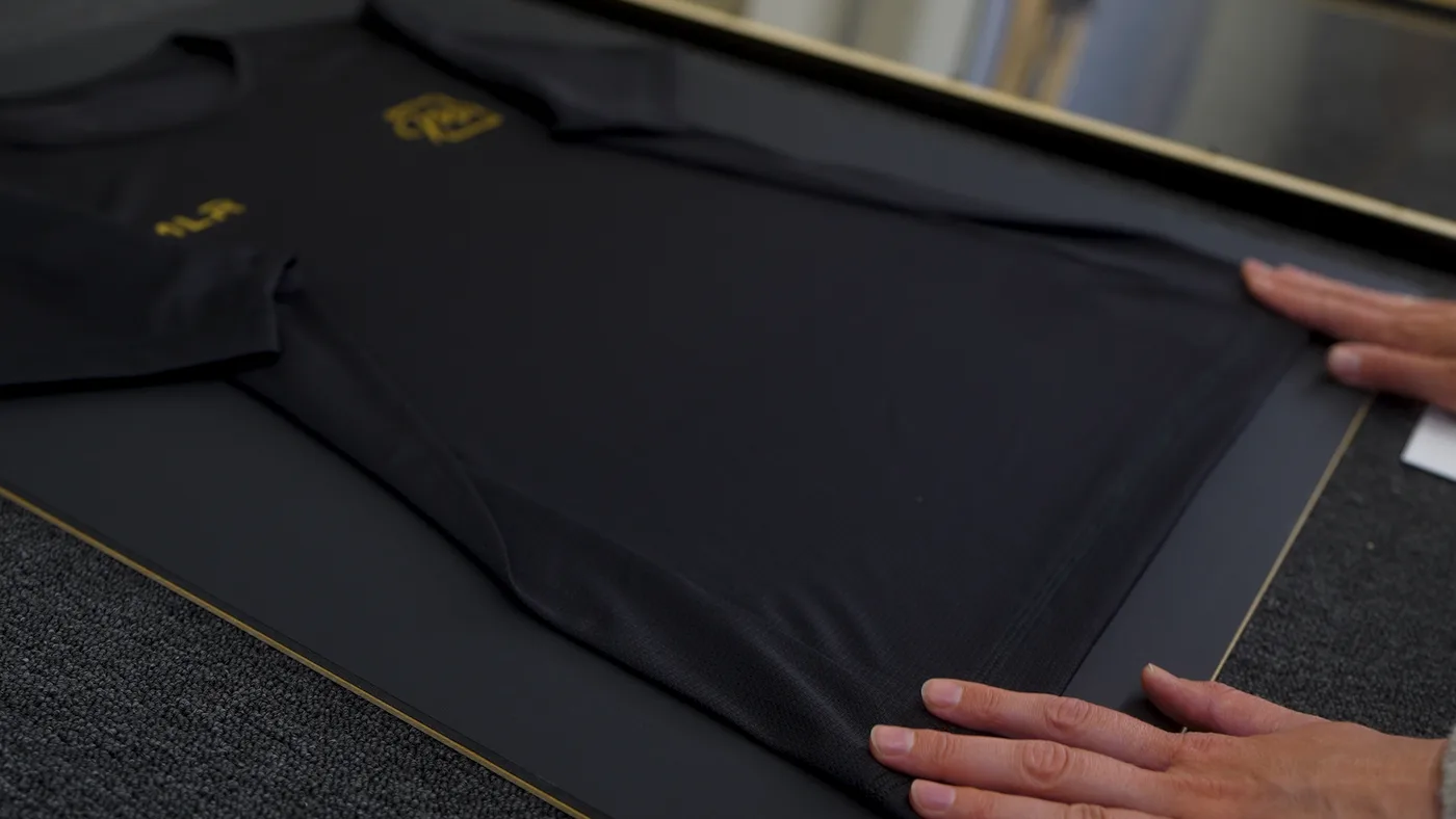Hände streichen das Trikot auf der Rückwand faltenfrei glatt